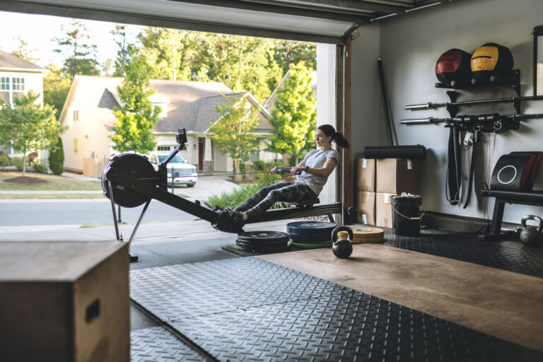 Active woman exercising on a rowing machine in her home garage gym during covid-19 pandemic