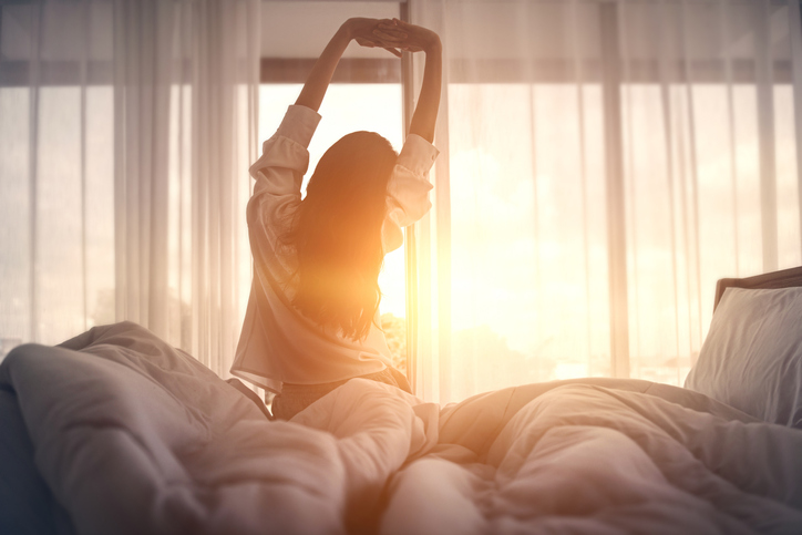Happy woman stretching in bed after waking up. Happy young girl greets good day